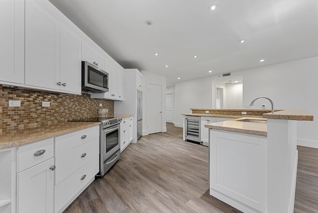 kitchen with sink, white cabinets, stainless steel appliances, a kitchen island with sink, and backsplash