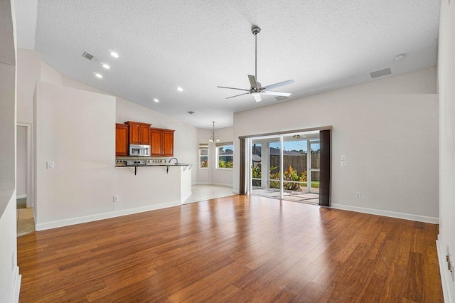 unfurnished living room featuring vaulted ceiling, ceiling fan, a textured ceiling, wood finished floors, and baseboards