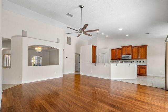 unfurnished living room with ceiling fan, light wood-type flooring, arched walkways, and visible vents