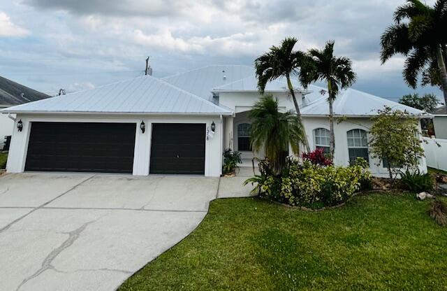 ranch-style house with a garage, driveway, metal roof, a front yard, and stucco siding