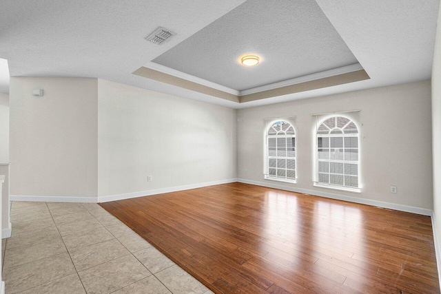 unfurnished room with a textured ceiling, wood finished floors, a raised ceiling, and visible vents