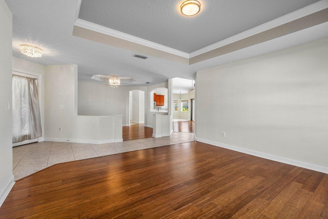 empty room with arched walkways, a raised ceiling, visible vents, and hardwood / wood-style floors