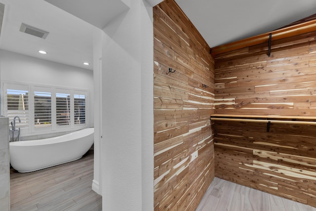 bathroom with a tub to relax in, hardwood / wood-style flooring, and wood walls