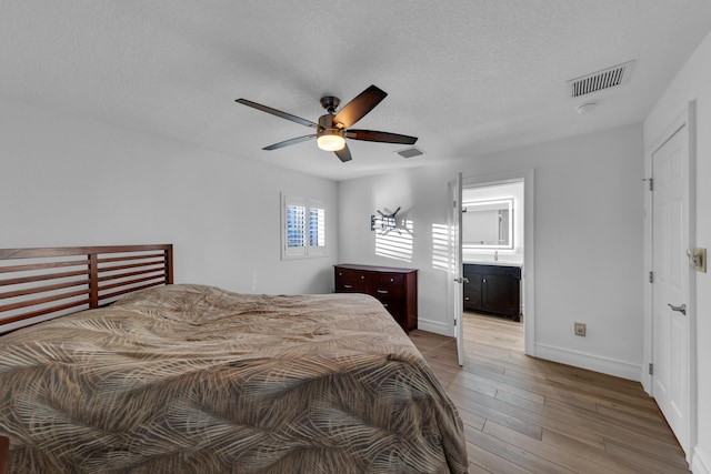 bedroom with ceiling fan, light hardwood / wood-style flooring, a textured ceiling, and ensuite bathroom