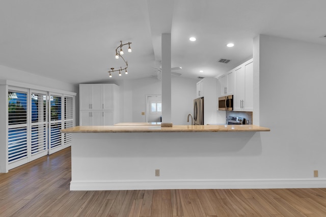 kitchen featuring vaulted ceiling, white cabinetry, kitchen peninsula, stainless steel appliances, and light wood-type flooring