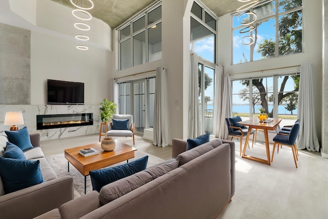 living room with a high ceiling, a water view, a fireplace, and light hardwood / wood-style floors