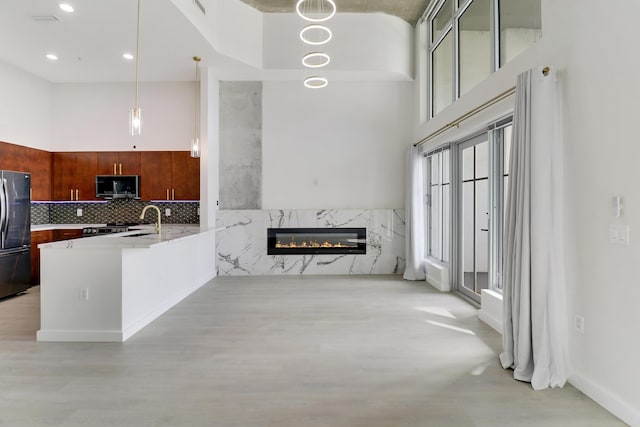 kitchen featuring hanging light fixtures, a towering ceiling, fridge, a high end fireplace, and kitchen peninsula