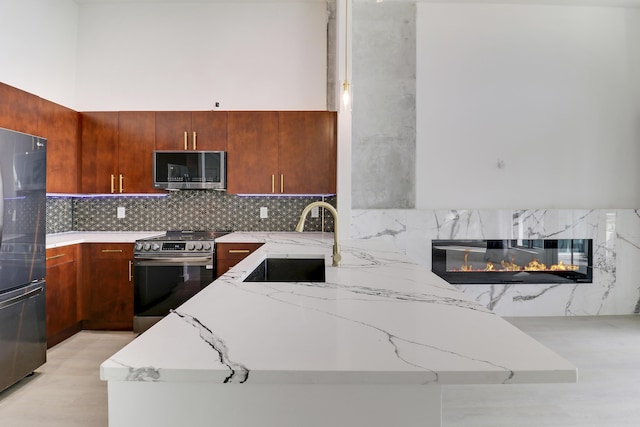 kitchen with sink, decorative backsplash, kitchen peninsula, stainless steel appliances, and a premium fireplace