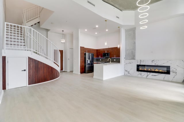 unfurnished living room with a notable chandelier, a high end fireplace, light hardwood / wood-style flooring, and a high ceiling