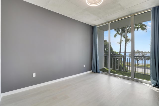 spare room featuring a water view, expansive windows, and light wood-type flooring