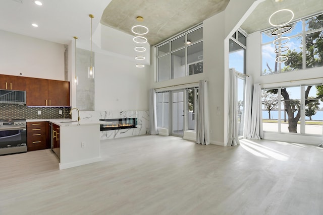 kitchen featuring a towering ceiling, decorative light fixtures, sink, stainless steel range, and light hardwood / wood-style flooring