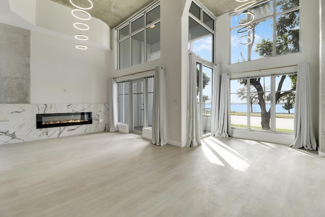 unfurnished living room featuring hardwood / wood-style floors, a towering ceiling, a high end fireplace, and a water view