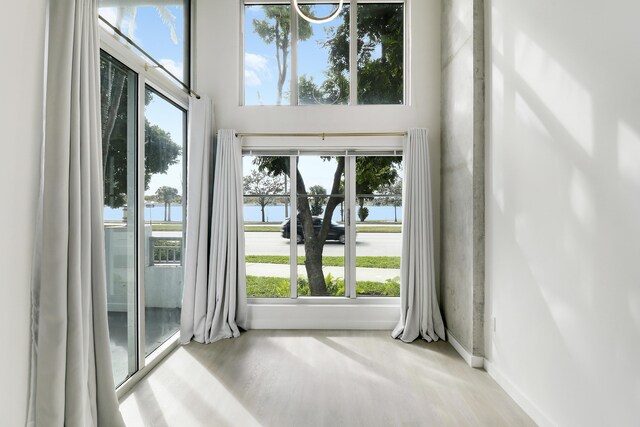 living room with a water view, a towering ceiling, a premium fireplace, and light hardwood / wood-style flooring