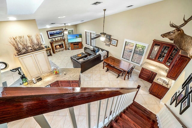 stairway featuring lofted ceiling, visible vents, ceiling fan, a lit fireplace, and tile patterned floors