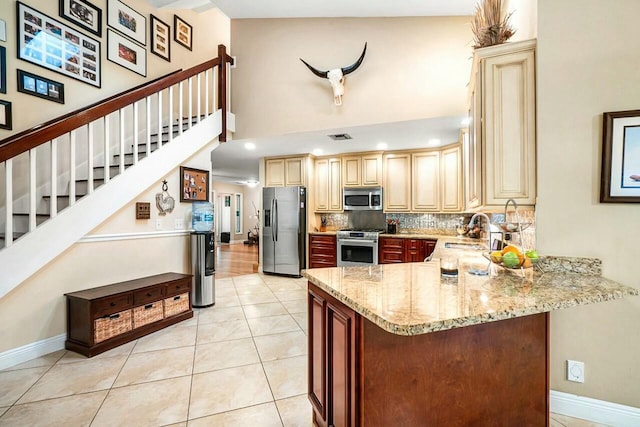 kitchen with tasteful backsplash, a high ceiling, appliances with stainless steel finishes, a sink, and light stone countertops