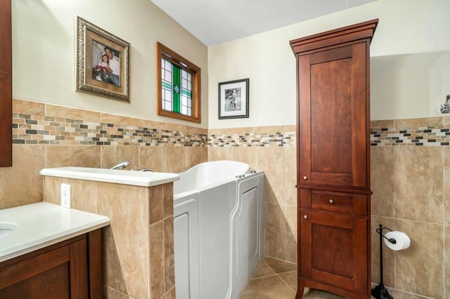 bathroom featuring tile walls, tile patterned flooring, a garden tub, and vanity