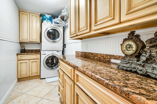 laundry area with light tile patterned floors, cabinet space, stacked washer / dryer, and wainscoting