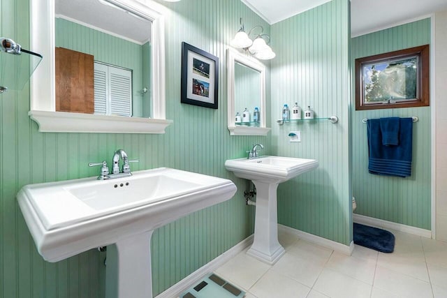 bathroom with baseboards, two sinks, toilet, tile patterned flooring, and crown molding