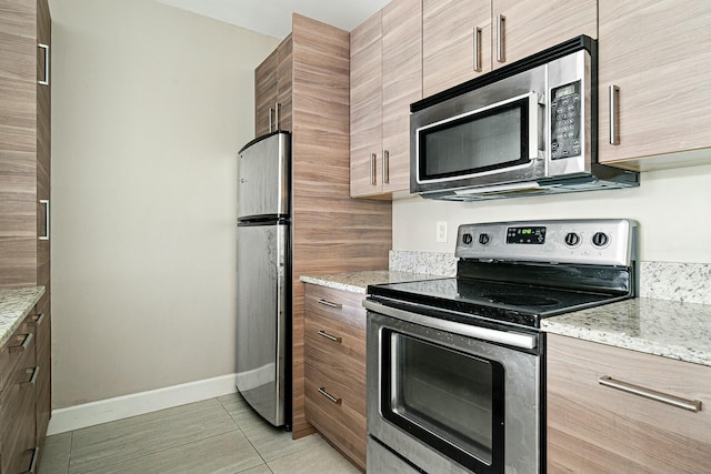 kitchen with stainless steel appliances, light tile patterned flooring, and light stone countertops