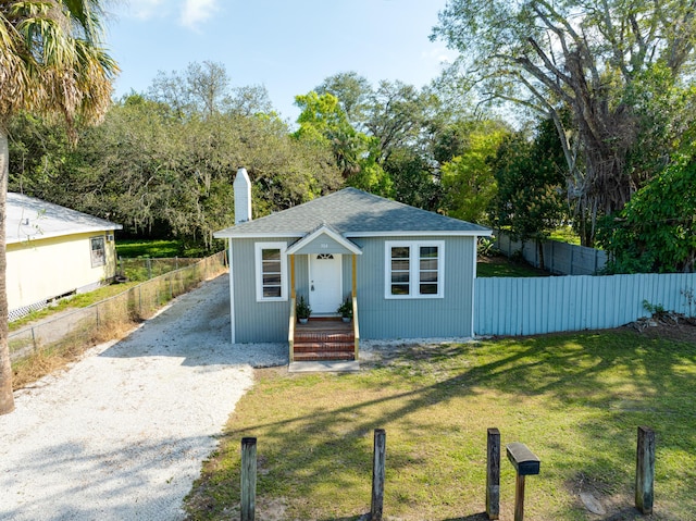 bungalow-style home featuring driveway, a chimney, fence, and a front yard