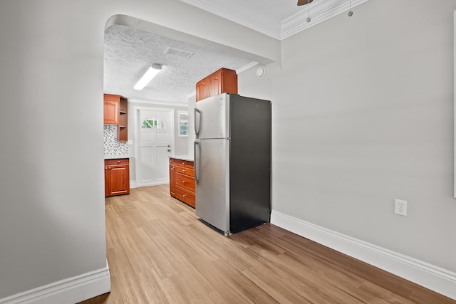 kitchen with stainless steel refrigerator, tasteful backsplash, ornamental molding, a textured ceiling, and light wood-type flooring