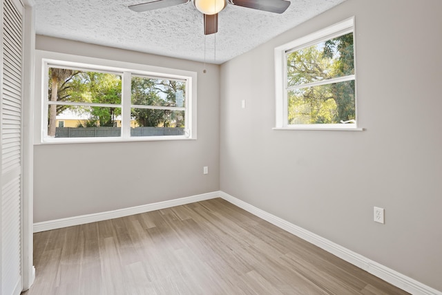 empty room with baseboards, a textured ceiling, plenty of natural light, and light wood-style floors