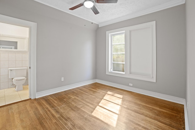 unfurnished bedroom featuring a textured ceiling, baseboards, connected bathroom, and light wood-style floors