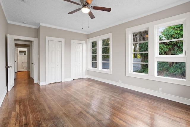 unfurnished bedroom with ornamental molding, dark hardwood / wood-style flooring, a textured ceiling, and two closets