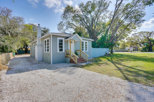 bungalow-style home featuring a front yard, driveway, fence, and a chimney