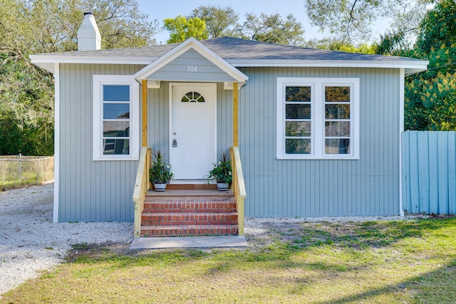 bungalow-style home featuring roof with shingles, fence, and a chimney