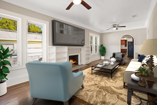 living area featuring arched walkways, wainscoting, plenty of natural light, and wood finished floors