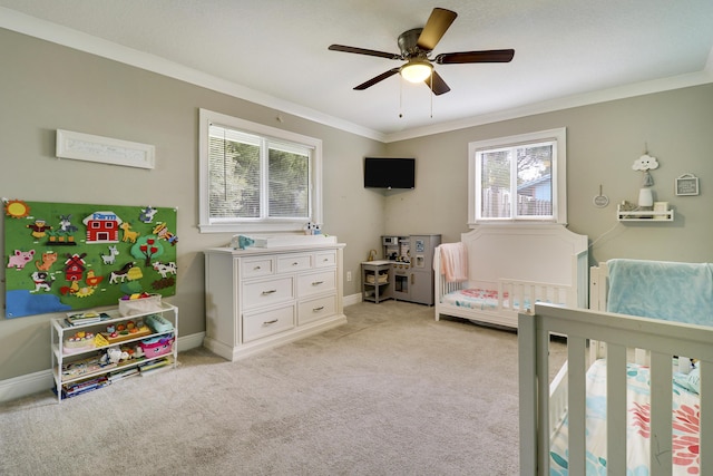 bedroom featuring ornamental molding, a nursery area, light carpet, and ceiling fan