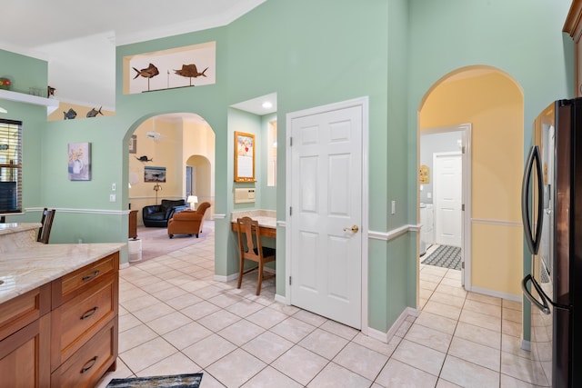 kitchen featuring light stone counters, a towering ceiling, refrigerator, and light tile patterned floors