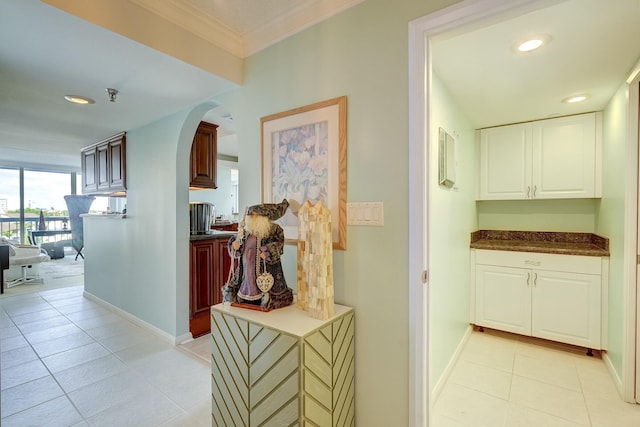 hallway with light tile patterned floors, baseboards, arched walkways, and ornamental molding