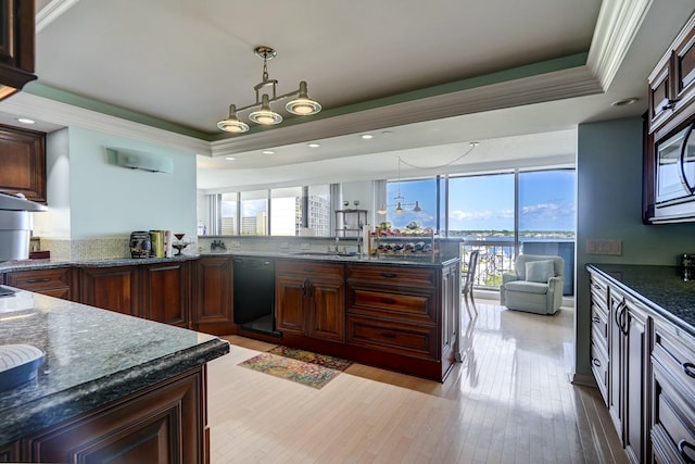 kitchen featuring a tray ceiling, crown molding, hanging light fixtures, light wood-style floors, and dark stone countertops