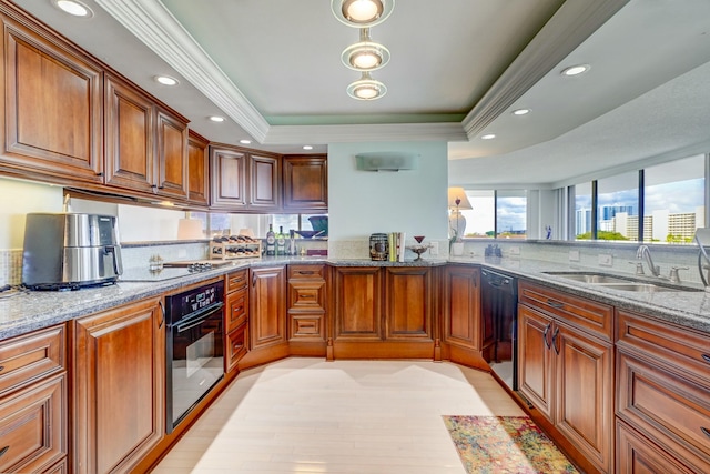 kitchen featuring a raised ceiling, brown cabinets, light stone countertops, black appliances, and a sink