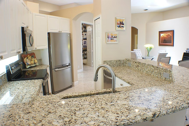 kitchen featuring light stone counters, appliances with stainless steel finishes, kitchen peninsula, and white cabinets