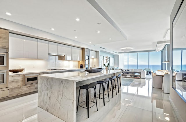 kitchen featuring a large island, a water view, light stone counters, stainless steel gas cooktop, and white cabinets