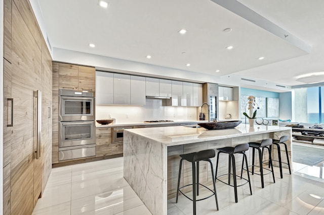 kitchen featuring white cabinetry, stainless steel appliances, light stone counters, a kitchen bar, and a large island with sink