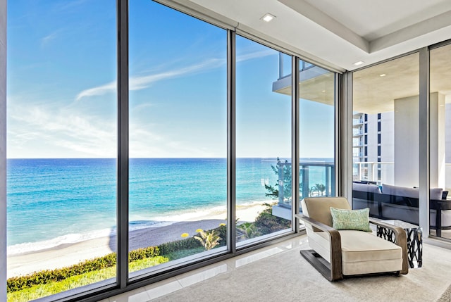 interior space featuring floor to ceiling windows, a water view, light colored carpet, and a beach view