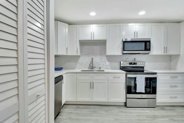 kitchen with white cabinetry, sink, backsplash, stainless steel appliances, and light wood-type flooring