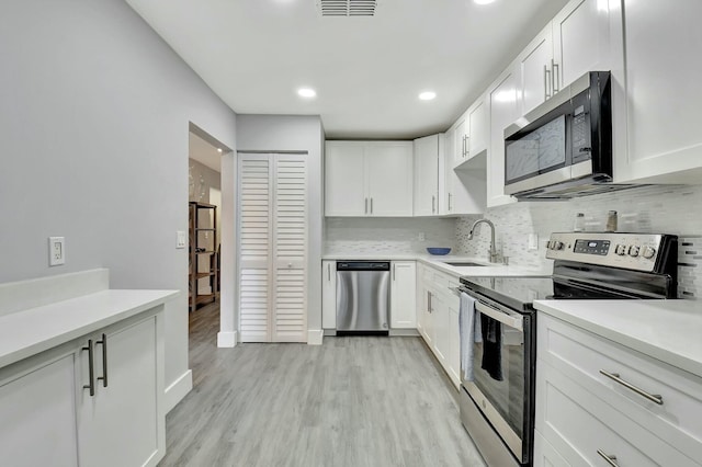 kitchen with appliances with stainless steel finishes, sink, backsplash, white cabinets, and light wood-type flooring