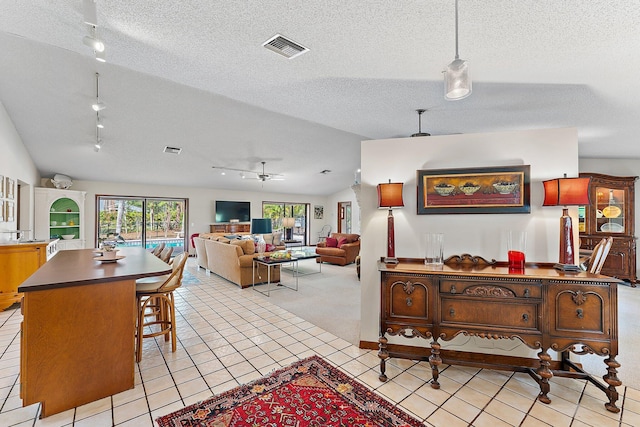 tiled living room with ceiling fan, track lighting, vaulted ceiling, and a textured ceiling