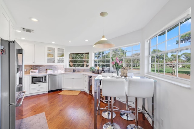 kitchen with sink, white cabinetry, pendant lighting, stainless steel appliances, and hardwood / wood-style floors