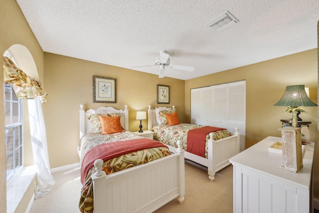 bedroom with light carpet, a textured ceiling, ceiling fan, and a closet