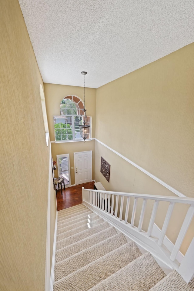 staircase featuring a textured ceiling and a chandelier