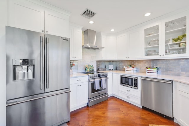 kitchen with white cabinetry, dark hardwood / wood-style flooring, stainless steel appliances, light stone countertops, and wall chimney range hood