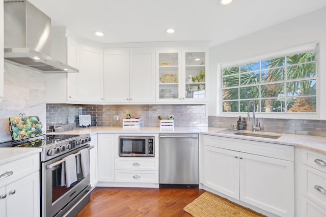 kitchen with wall chimney range hood, sink, appliances with stainless steel finishes, white cabinetry, and wood-type flooring