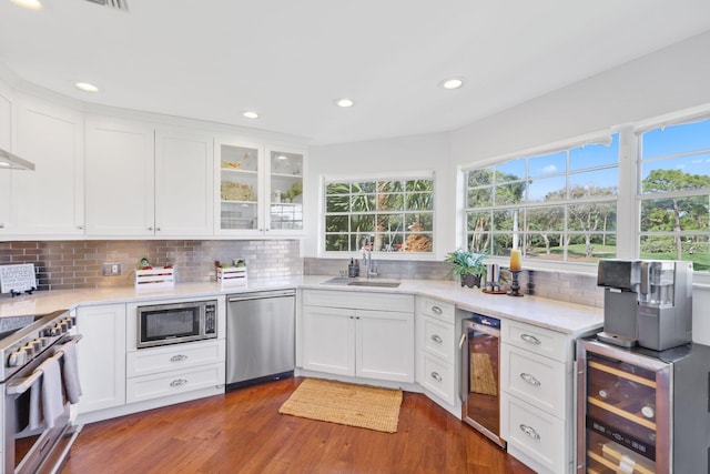 kitchen with sink, beverage cooler, white cabinets, and appliances with stainless steel finishes