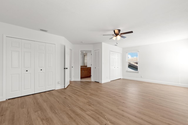 interior space with two closets, ensuite bath, ceiling fan, and light wood-type flooring